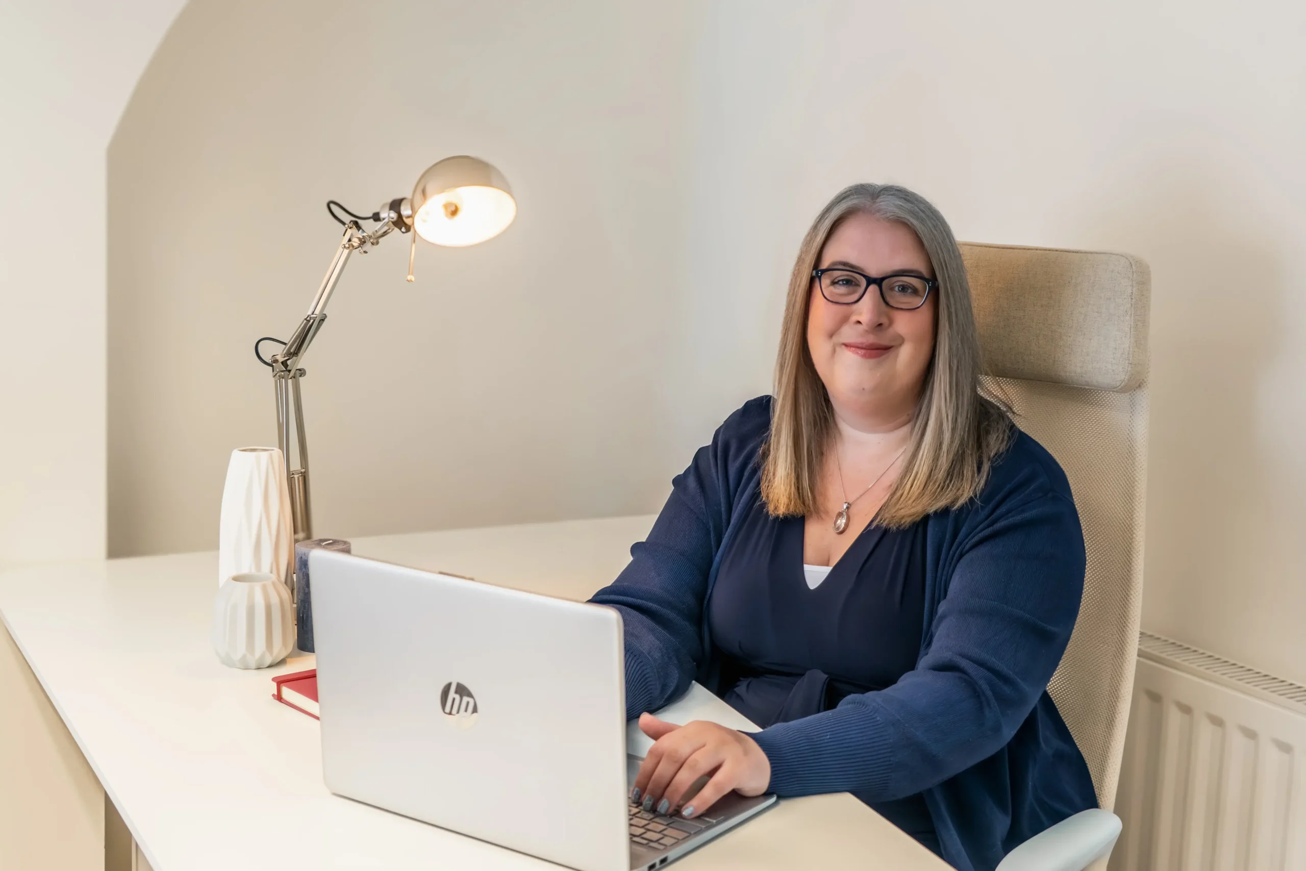 Hannah Paskin working at her desk with a laptop and lamp.