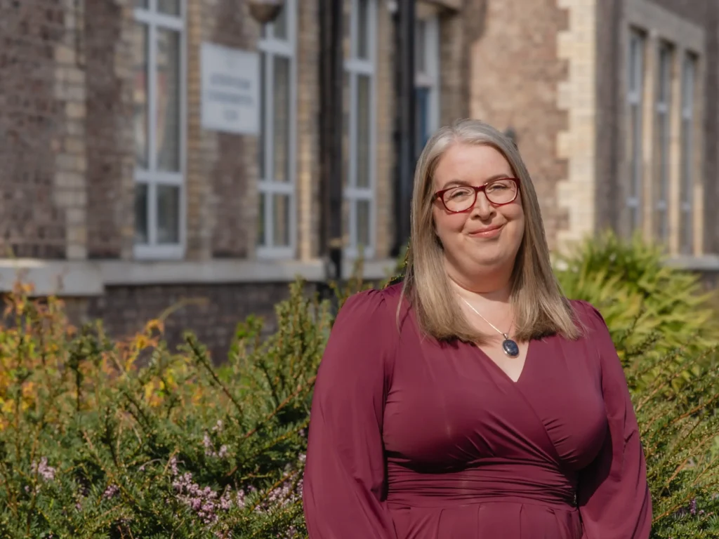 Hannah Paskin in a garden setting with flowers and a brick building behind her.