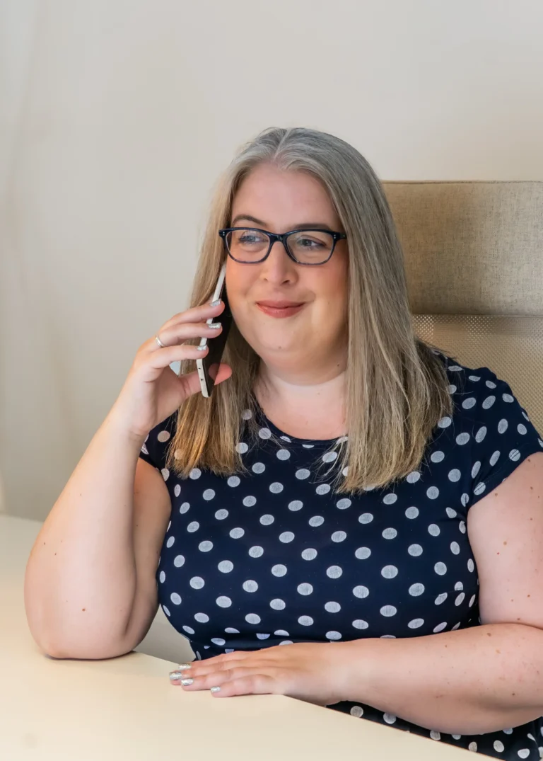Hannah Paskin with glasses in an office setting, speaking on the phone with a pleasant expression.