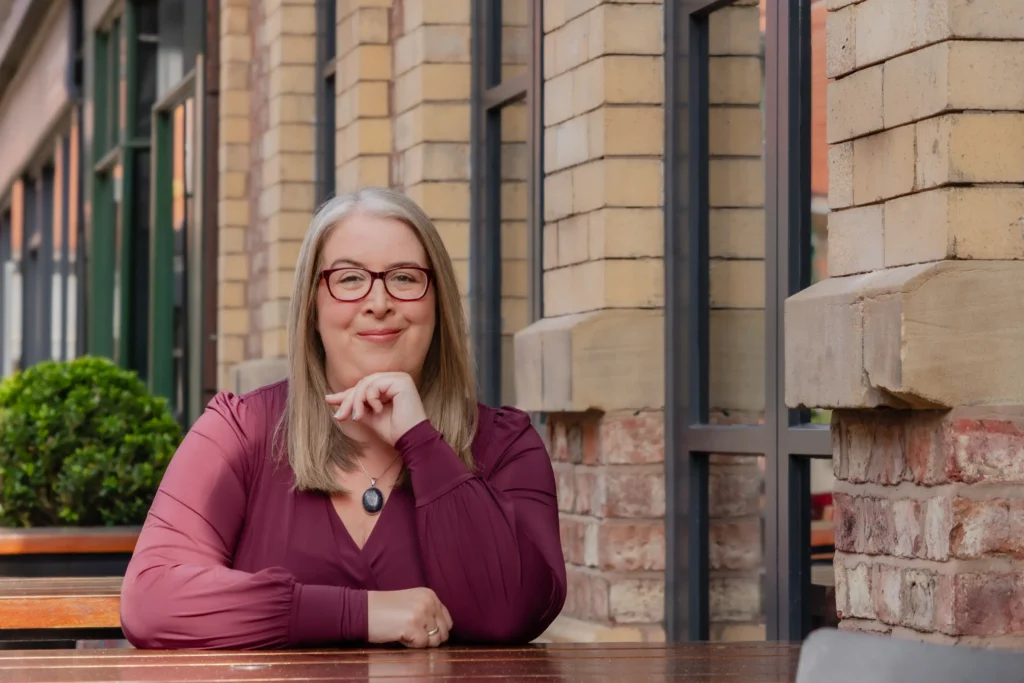Hannah Paskin against a brick and glass urban background, exuding confidence and warmth.