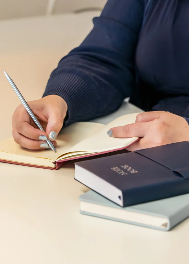 Close-up of a hand writing in a notebook with a silver pen.